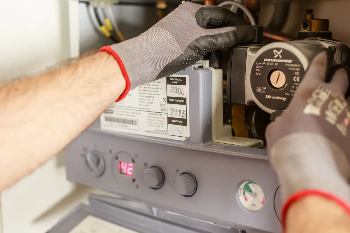 Gloved hands adjusting a boiler pump beneath the casing