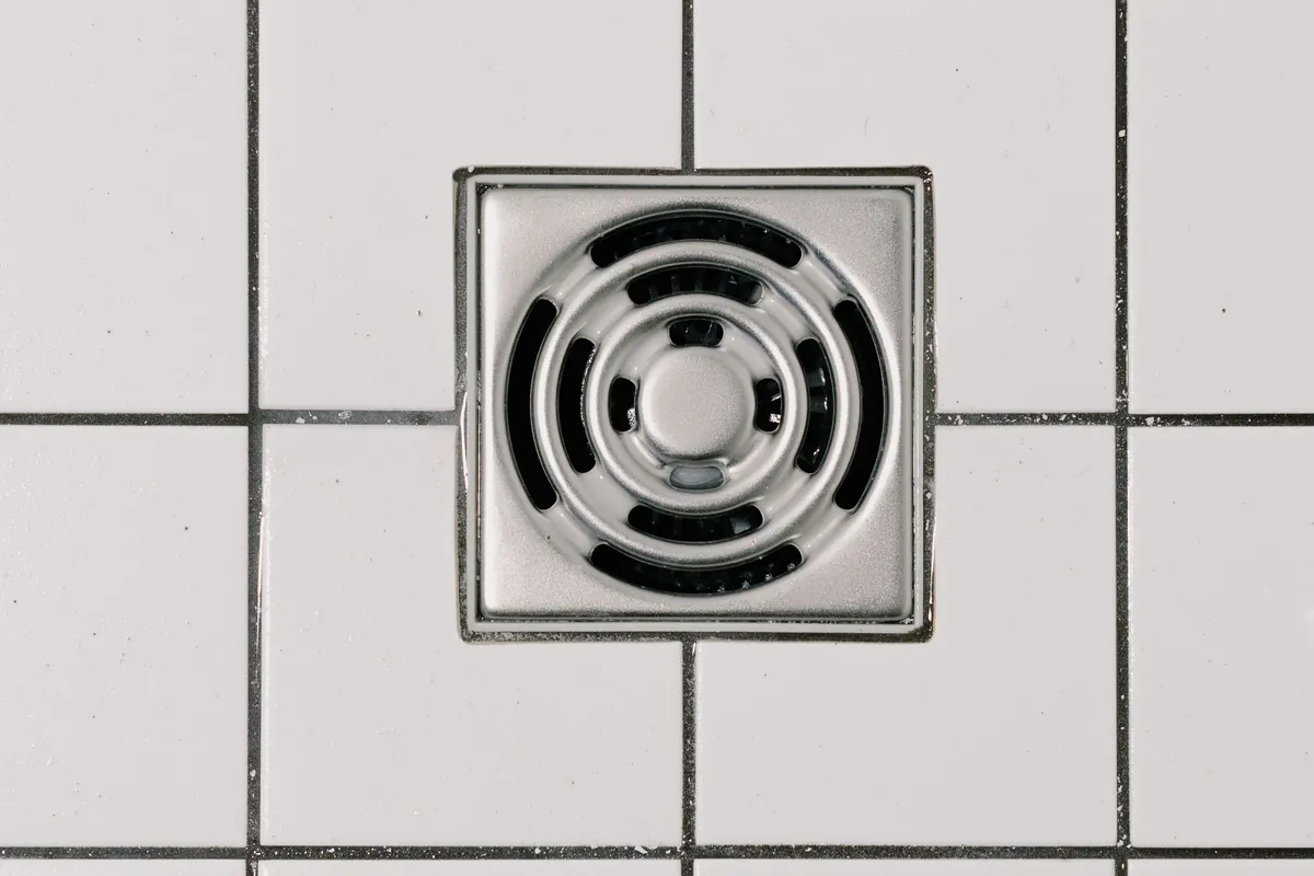 Square shower drain set into white tiles